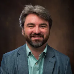 Profile photo of a smiling, bearded man