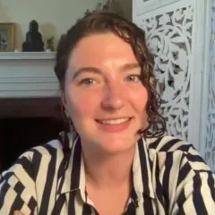 Video frame of Alexandra Kralick smiling while sitting in front of a fireplace.