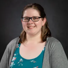 woman with brown hair and glasses wearing a grey sweater