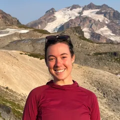 A woman with light skin tone in a red shirt in front of mountains