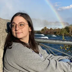 image of woman wearing glasses and grey sweater in front of ocean