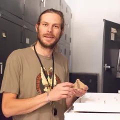man with beard in brown shirt holding fossil plant