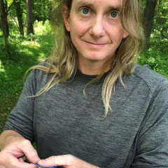 A man with light skin tone and long hair in a gray shirt holds a blue bird