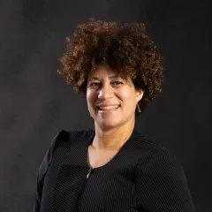 A headshot of an African American woman looking at the camera with a dark background. 