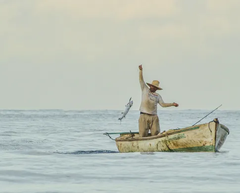 A fisherman casting a net from a small boat on the ocean. 