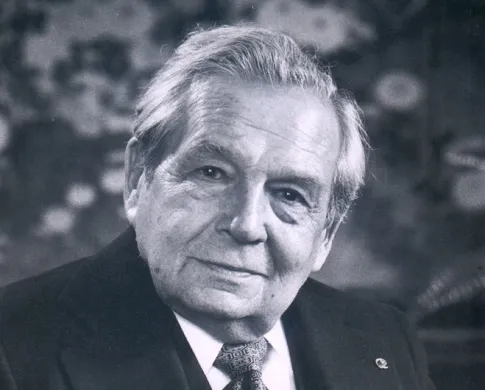 Portrait of a light-skinned man in a suit holding a pair of glasses