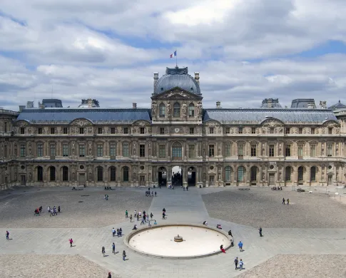 People milling on a stone plaza in front of the Louvre