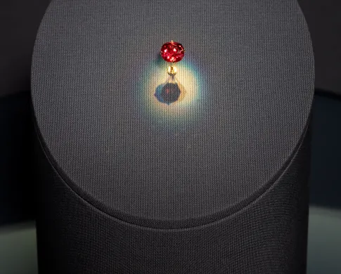 A spotlit red diamond gem mounted on a gray circular pedestal