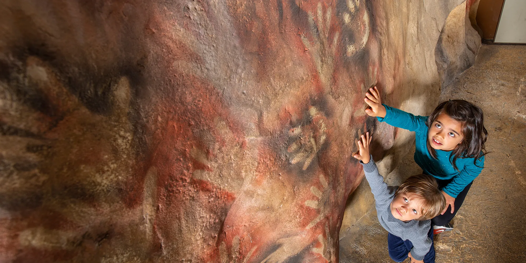 Two children put their hands on a mural at the Museum.