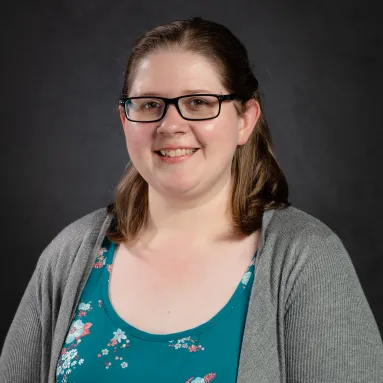 woman with brown hair and glasses wearing a grey sweater