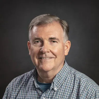A man with light skin tone and gray hair in a blue plaid shirt