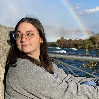 image of woman wearing glasses and grey sweater in front of ocean