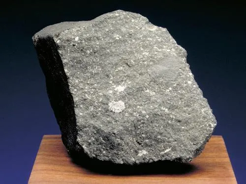 Allende Meteorite - a rock with sharp edges displayed on a wood surface