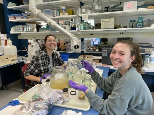 Two women sitting at a desk with many jars of invertebrate research specimens