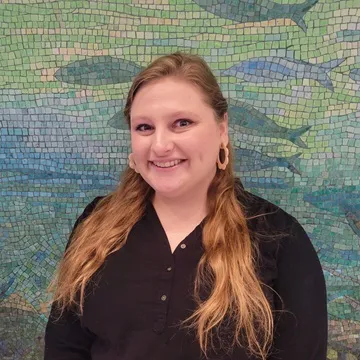 Jamie Thompson smiling in front of a mosaic artwork