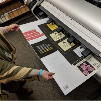 A large poster coming out of a printer being grabbed by two hands 