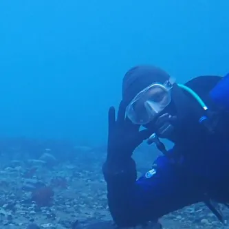 A scuba diver rests his elbow and leg on the sea floor next to a data logger tethered to a weight on the bottom.