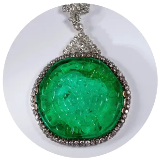 A round green gem surrounded by diamonds on a necklace. 