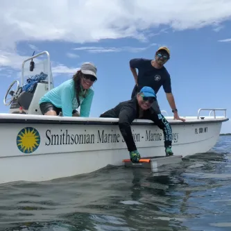 Three researchers on a Smithsonian Institution research vessel collect ocean monitoring equipment from the ocean