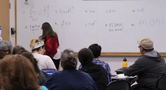 Group of people looking at a white board with a woman writing.