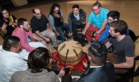 Group of people sitting around and playing a Powwow drum.