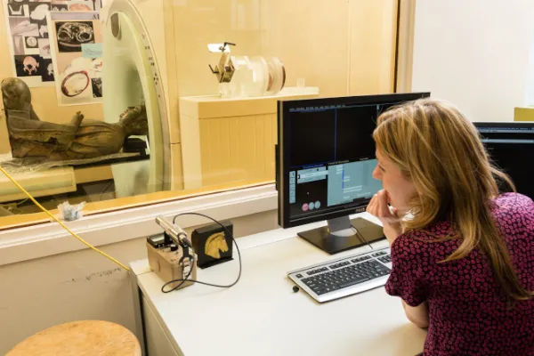 Scientist at computer, watching sculpture go into CT scanner