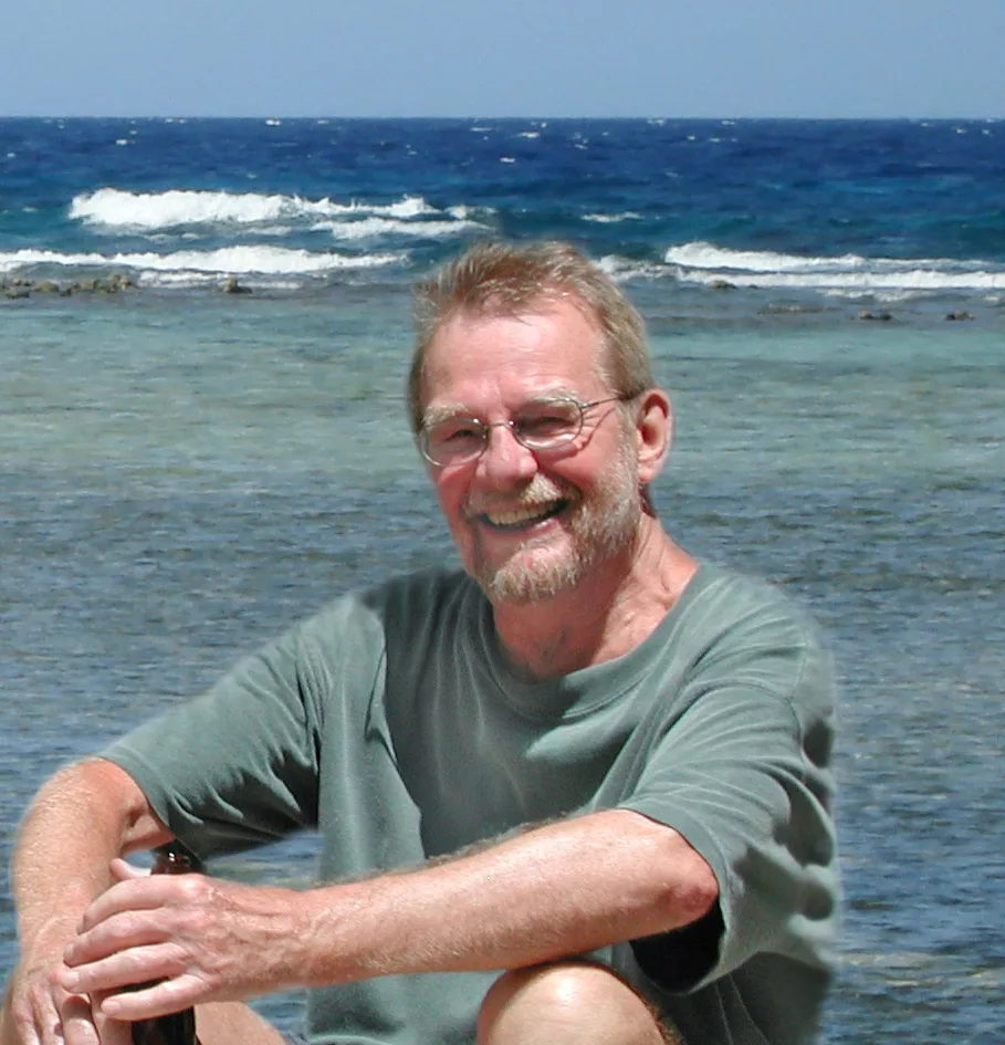 A man sitting down on the beach with the ocean behind him