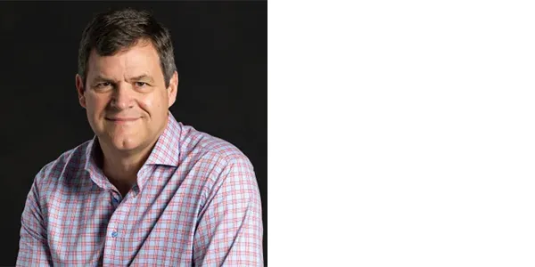 A headshot of Kirk Johnson, a light-skinned man with short brown hair wearing a blue and red gingham button-up shirt.	