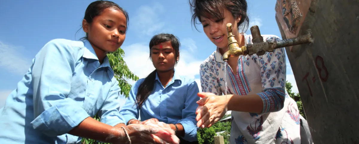 a group of three girls washing hands at a water spicket
